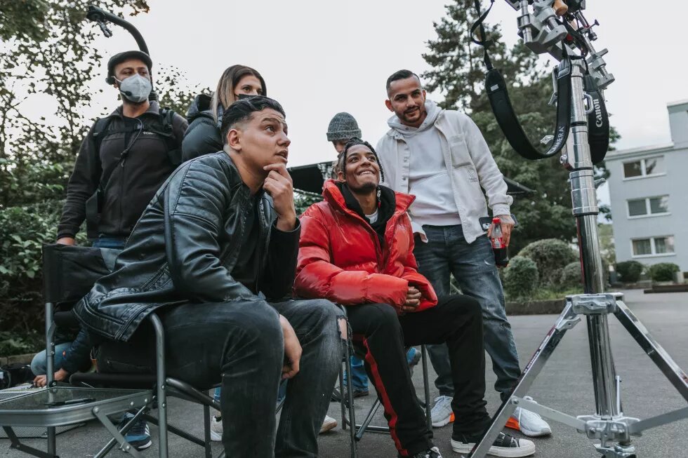 Foto am Set von der Serie Hype: Eine Gruppe von Darsteller*innen und der Filmcrew schauen gemeinsam auf einen Monitor